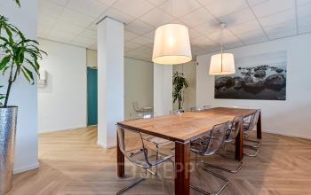 Kantoorruimte huren op Fonteinlaan 5 in Haarlem Zuid. Moderne, lichte ruimte met grote houten tafel en stoelen, beige muren, en planten, ideaal voor vergaderingen.