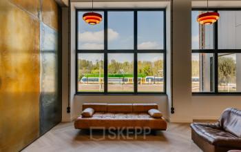 Stijlvolle kantoorruimte huren op Haarlemmerstraatweg 13, Halfweg, met een licht interieur en comfortabele leren banken. Grote ramen bieden uitzicht op de omgeving, ideaal voor inspirerende werkmomenten.