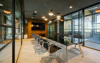 Moderne vergaderruimte in een kantoorpand aan de Haarlemmerstraatweg 13, Halfweg, met een glazen wand, zwarte stoelen en een grote tafel, ideaal om kantoorruimte te huren.