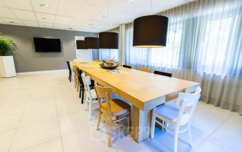 Heldere kantoorruimte aan Herenweg 115, Heemstede met lange houten tafel, stoelen en moderne hanglampen, ideaal voor vergaderingen of teamwerk. Beschikbare kantoorruimte huren biedt frisse en functionele werkplekken.