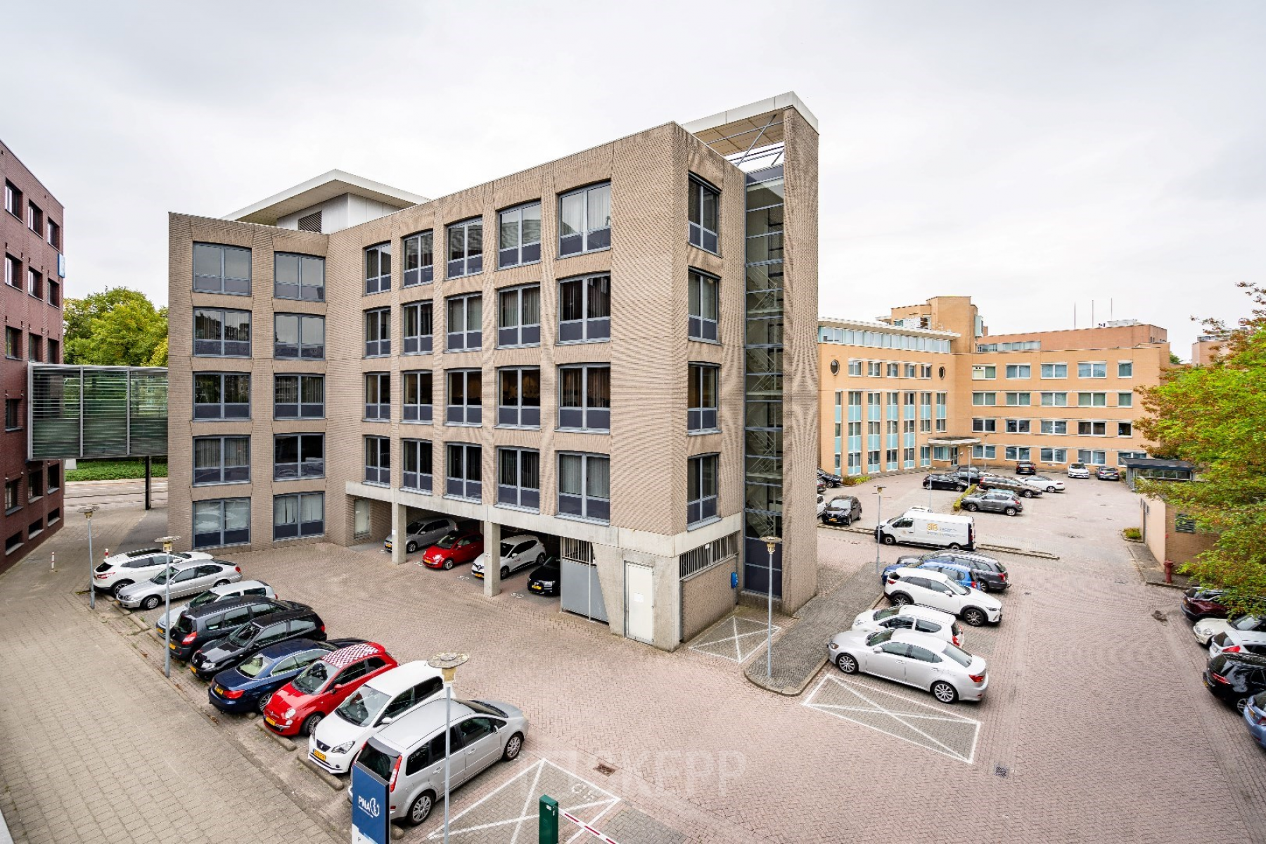 Uitzicht op het kantoorpand aan Geerstraat 115 in Heerlen, met meerdere geparkeerde auto's op de voorgrond. Kantoorruimte huren beschikbaar in dit moderne gebouw.