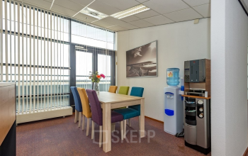 Kantoorruimte huren aan de Milaanstraat 70-110 in Heerlen met kleurrijke stoelen rondom een houten tafel, waterkoeler en koffiezetapparaat.