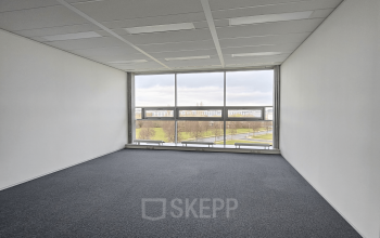 Kantoorruimte huren in Snellius 1, Heerlen. Leeg kantoorpand met groot raam dat uitzicht biedt op een rustige omgeving.