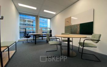 Kantoorruimte huren in Snellius 1, Heerlen: modern ingericht kantoor met ronde tafel, stoelen en groot raam met uitzicht op kantoorpand.