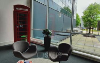 Kantoorruimte huren in een modern kantoorpand op Snellius 1, Heerlen, met grote ramen en een gezellige zithoek. Twee stoelen staan bij een lage tafel met tijdschriften en een kleurrijke telefooncel.