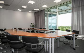 Vergaderruimte in het kantoorpand op Snellius 1, Heerlen met U-vormige tafel en stoelen, grote ramen met uitzicht op omgeving.