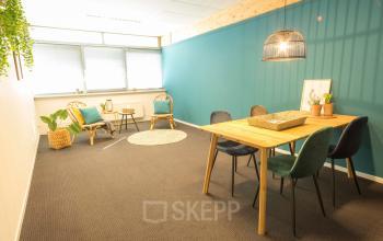 Kantoorruimte huren in Helmond, Steenovenweg 5. Ruim en licht kantoor met blauw-groene muur, houten tafel en comfortabele stoelen.
