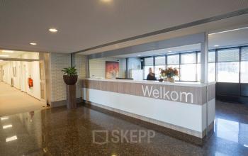 Ingang van kantoorpand aan Steenovenweg 5 in Helmond met 'Welkom' balie en zakelijke activiteit van receptioniste.