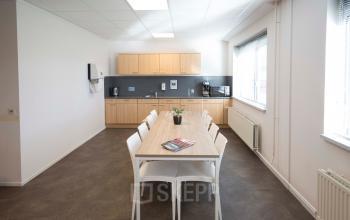 Kantine in kantoorpand Steenovenweg 5, Helmond, met houten tafels en stoelen, lichte kleurstelling en een moderne keukenwand.