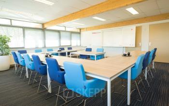Moderne kantoorpand op Steenovenweg 5, Helmond met vergadertafel en blauwe stoelen. Groot raam voor natuurlijk licht. Ideaal voor kantoorruimte huren.