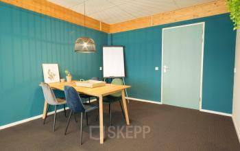 Vergaderruimte te huur op Steenovenweg 5, Helmond. Donkergroene muur met houten tafel, vier stoelen, flipover en hanglamp.
