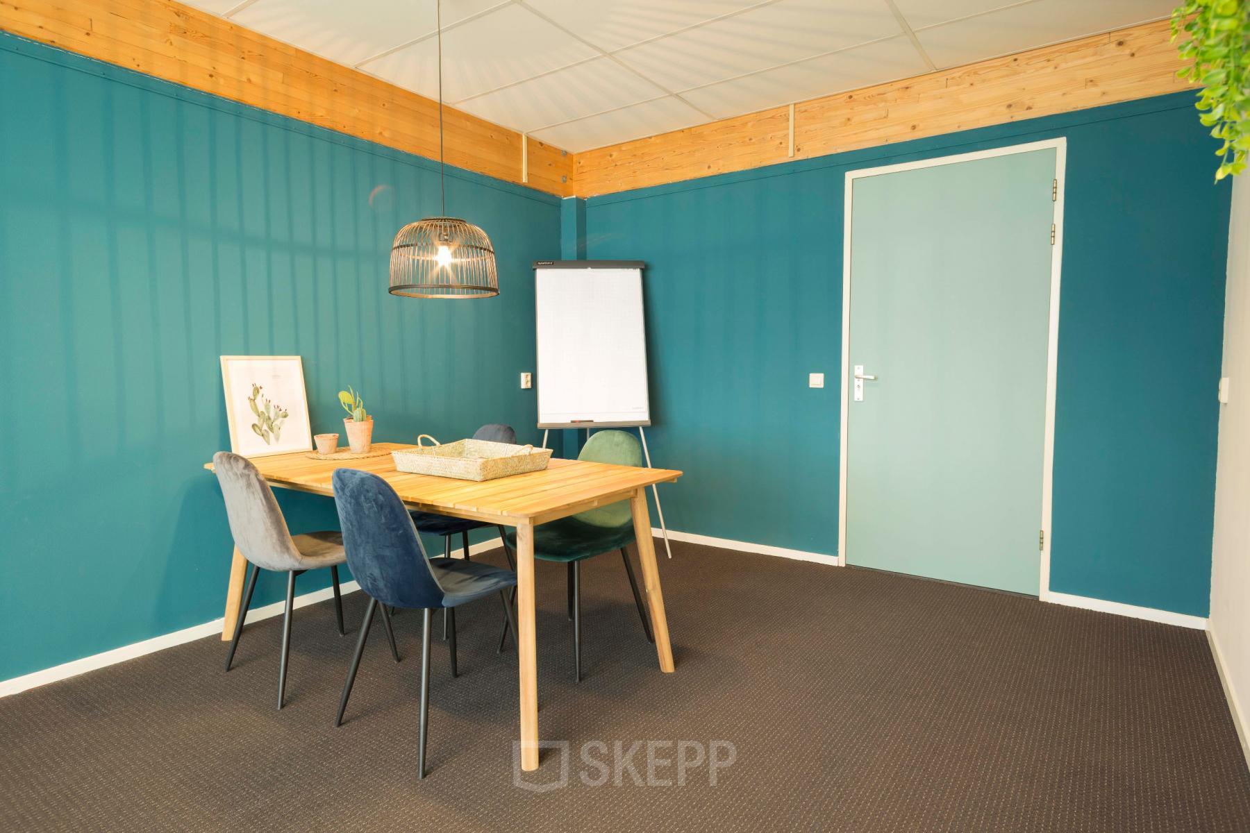 Vergaderruimte te huur op Steenovenweg 5, Helmond. Donkergroene muur met houten tafel, vier stoelen, flipover en hanglamp.