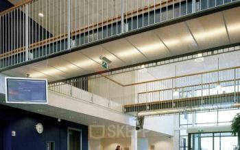 Ruime, lichte ontvangsthal in kantoorpand op Jan Tinbergenstraat 202, Hengelo. Een persoon zit achter de receptiebalie. Ideaal voor bedrijven die kantoorruimte willen huren in een moderne omgeving.