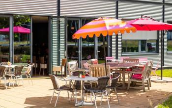 Buitenterras met kleurrijke parasols en diverse zitplaatsen aan Jan Tinbergenstraat 202, ideaal voor een pauze tijdens het kantoorruimte huren in Hengelo.