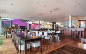 Ruime kantoorruimte aan Jan Tinbergenstraat 202, Hengelo met grote tafels, moderne verlichting en bar, ideaal om te huren voor vergaderingen of informeel overleg tussen collega's.