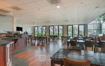 Binnen in kantoorpand Jan Tinbergenstraat 202, Hengelo zie je een ruime, gemeubileerde open vloerplan met veel natuurlijk licht en houten tafels. Ideaal voor werkruimte huren. Grote ramen bieden uitzicht op de stad.