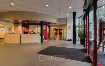Ruime en moderne receptie van het kantoorpand aan Lansinkesweg 4, Hengelo. Personen aan de balie verzorgen receptiewerkzaamheden. Grote ramen zorgen voor natuurlijke lichtinval, ideaal voor kantoorruimte huren.