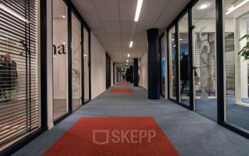 Kantoorpand aan Lansinkesweg 4, Hengelo met een modern ingerichte gang en glazen wanden met zicht op verschillende kantoren. Heldere verlichting en kleurrijke vloerbedekking.