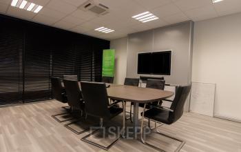 Moderne vergaderruimte in kantoor op Lansinkesweg 4, Hengelo met grote tafel, acht stoelen, muur-TV en whiteboard.
