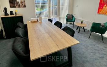 Kantoorruimte huren aan Hamerstraat 10 in Hengelo, met een lichte vergaderruimte voorzien van een lange tafel, stoelen en kunst aan de muur. Grote ramen zorgen voor veel natuurlijk licht.