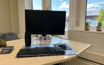 Kantoorruimte huren op Hamerstraat 10 in Hengelo met modern bureau, computerscherm en toetsenbord bij raam, uitzicht op blauwe lucht en groen buiten.