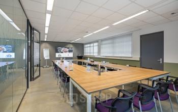 Vergaderruimte in kantoorpand op Demmersweg 21 - 37, Hengelo. Ingericht met grote tafels en stoelen, geschikt voor zakelijke bijeenkomsten. Grote ramen zorgen voor veel natuurlijk licht.