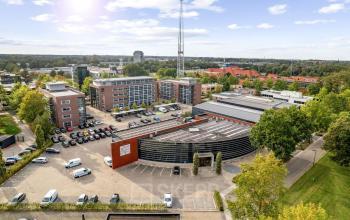 Luchtfoto van het kantoorpand op Lintelerweg 40 in Hengelo, omgeven door parkeerplaatsen en groene bomen. Ideale locatie voor kantoorruimte huren in een levendige omgeving.