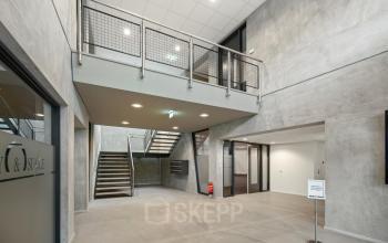 Entree van modern kantoorpand op Lintelerweg 40, Hengelo. Ruime hal met industriële uitstraling en zicht op de trap. Ideaal voor bedrijven die kantoorruimte willen huren.