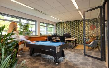 Kantoor met grote ramen, biljarttafel en werkplekken aan Demmersweg 41-47 in Hengelo. Persoon speelt biljart terwijl anderen aan het werk zijn.