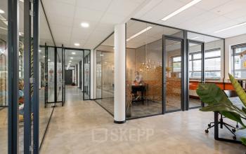 Moderne kantoorruimte te huur aan Demmersweg 41-47 in Hengelo met glazen wanden, stijlvolle inrichting en een medewerker die aan het werk is in een afgesloten kantoor.