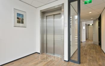 Kantoorruimte huren in Hengelo aan de Welbergweg 60 met nette entree met lift en houten vloer. Het licht binnendringt door een glazen wand, terwijl kunst aan de muur zorgt voor een stijlvolle touch.