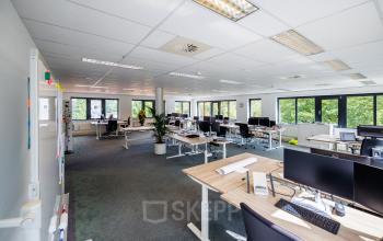 Moderne kantoorruimte met ruime opstelling van bureaus en computerschermen, veel natuurlijk licht en groene elementen aan de Welbergweg 60 in Hengelo. Geschikt voor wie kantoorruimte wil huren.