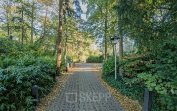 Buitenzicht van een kantoorpand gelegen aan de Mozartlaan 25 in Hilversum, omgeven door groen en een geplaveide oprit in een rustige omgeving.