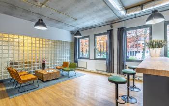 Moderne kantoorruimte op Mozartlaan 25 in Hilversum met stijlvolle zitgedeelte en houten tafel. Grote ramen bieden uitzicht op de straat. Lampen verlichten de vergaderruimte. Ideaal voor kantoorruimte huren.