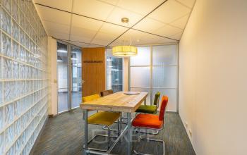 Vergaderruimte in kantoorpand op Mozartlaan 25 in Hilversum met houten tafel en kleurrijke stoelen, ideaal voor wie kantoorruimte wil huren.