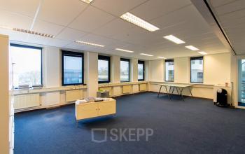 Lichte kantoorruimte op Franciscusweg 219 in Hilversum met blauwe vloerbedekking, grote ramen en enkele tafels voor zakelijke activiteiten, klaar voor verhuur.