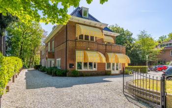 Kantoorpand Utrechtseweg 47 in Hilversum met een charmante uitstraling, omringd door groene bomen en zonnige ramen. Ideale plek om een kantoorruimte te huren.