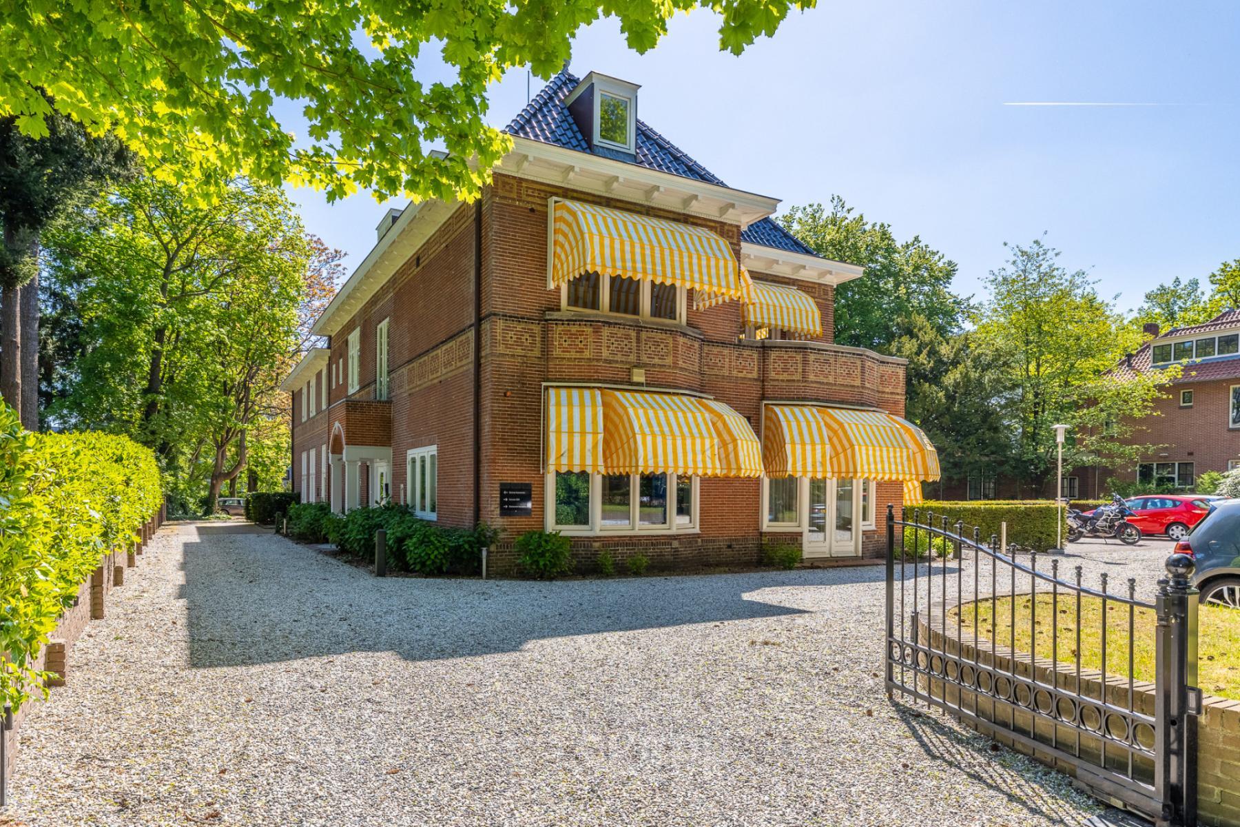 Kantoorpand Utrechtseweg 47 in Hilversum met een charmante uitstraling, omringd door groene bomen en zonnige ramen. Ideale plek om een kantoorruimte te huren.