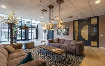 Stijlvolle ontvangstruimte binnen kantoorpand Marathon 2 in Hilversum, met comfortabele banken, moderne verlichting en decoratieve elementen. Perfect voor wie een kantoorruimte wil huren.