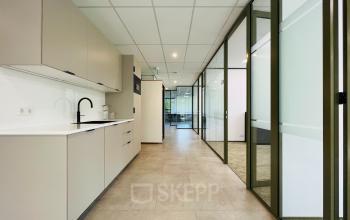 Moderne kantoorruimte te huur in Hilversum met glazen wanden en een kitchenette. De ruimte is licht en praktisch voor diverse zakelijke activiteiten.