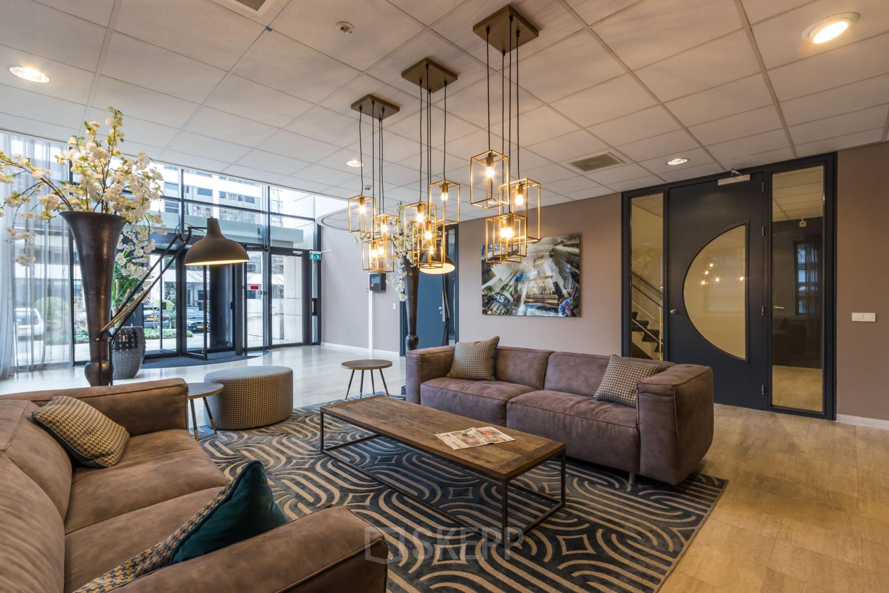 Stijlvolle ontvangstruimte binnen kantoorpand Marathon 2 in Hilversum, met comfortabele banken, moderne verlichting en decoratieve elementen. Perfect voor wie een kantoorruimte wil huren.