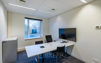Kantoorruimte huren aan Olympia 4 in Hilversum met moderne werktafel, comfortabele stoelen en een grote monitor aan de muur. Ideaal voor productieve zakelijke bijeenkomsten.
