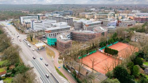 Luchtfoto van het moderne kantoorgebouw op Olympia 4 in Hilversum, nabij een kruispunt en naast tennisbanen, ideaal voor huur als kantoorruimte.