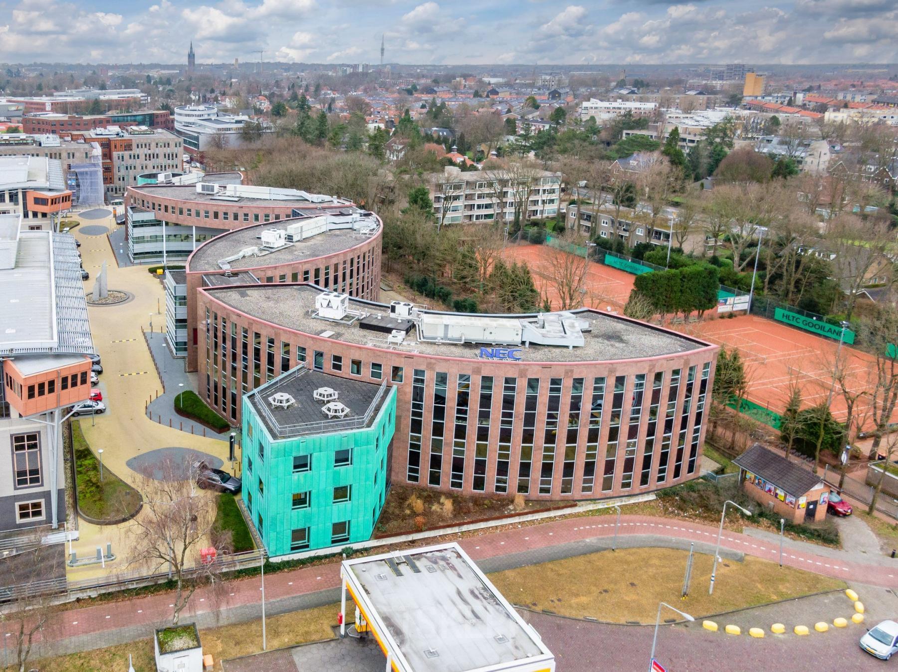 Buitenaanzicht van een modern kantoorpand aan Olympia 4, Hilversum. Het gebouw heeft een opvallend gebogen ontwerp en biedt ruimte voor bedrijven die kantoor willen huren in een levendige omgeving.