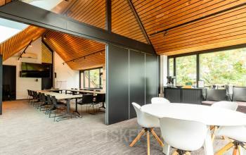 Ruime en lichte kantoorpand op Steijnlaan 16, Hilversum met moderne inrichting en houten accenten, ideaal voor kantoorruimte huren met open werkplekken en een vergadertafel bij het raam.