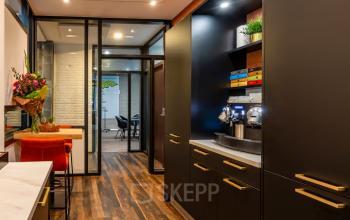 Moderne kantoorruimte met houten vloeren en strakke afwerking op Steijnlaan 16, Hilversum. De ruimte is gemeubileerd met tafels en stoelen, ideaal voor kantoorruimte huren. Een glazen wand scheidt verschillende werkruimtes.