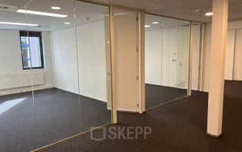 Leeg kantoorpand op Catharina van Renneslaan 8-10 in Hilversum, met glazen wanden en grijze vloerbedekking. Ideaal voor bedrijven die kantoorruimte willen huren in een lichte omgeving.