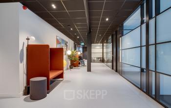 Moderne gang in een kantoorpand aan De Wel 20 in Hoevelaken met stijlvolle zitplekken en glazen wanden, ideaal voor wie kantoorruimte wil huren.