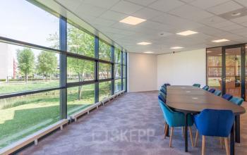 Vergaderruimte in kantoorpand op Polarisavenue 130-150, Hoofddorp met lange tafel en kleurrijke stoelen. Grote ramen met uitzicht op groene omgeving.