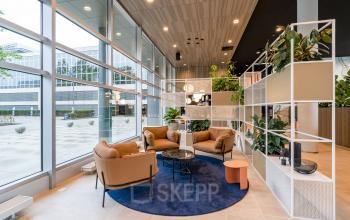 Moderne, lichte lobby met grote ramen en stijlvolle meubels in kantoorpand op Polarisavenue 1, Hoofddorp. Planten en comfortabele zitplaatsen aanwezig.